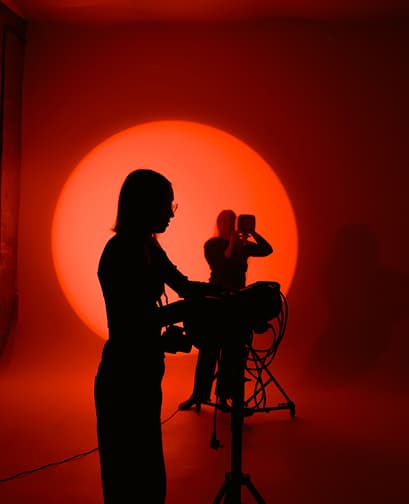 Silhouette of a person operating a camera against a bright red circular light backdrop